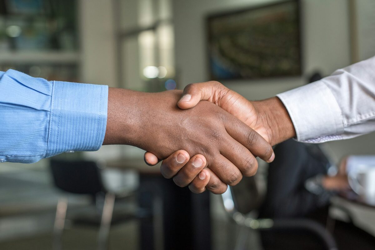 Aperto de mão entre dois profissionais de terno em mesa de reunião, simbolizando o fechamento de contrato com captador de projetos esportivos