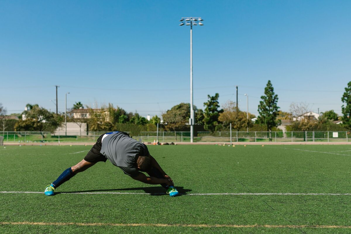 Atleta faz alongamento no campo ao entardecer