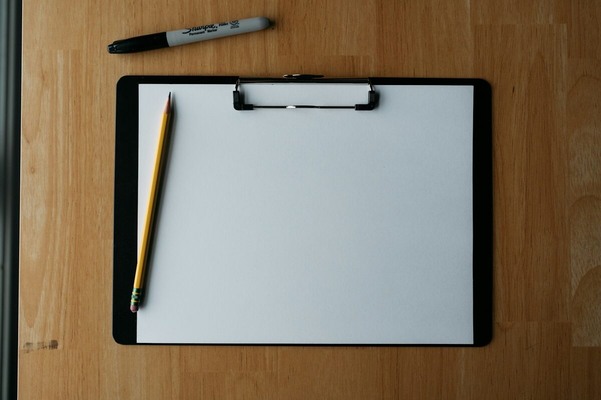Prancheta com folha em branco, lapis e marcador sobre mesa de madeira