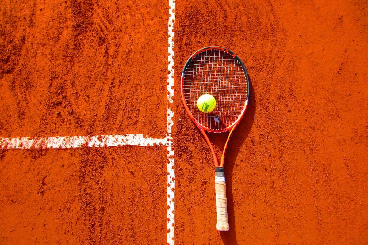 Raquete e bola sobre o saibro alaranjado